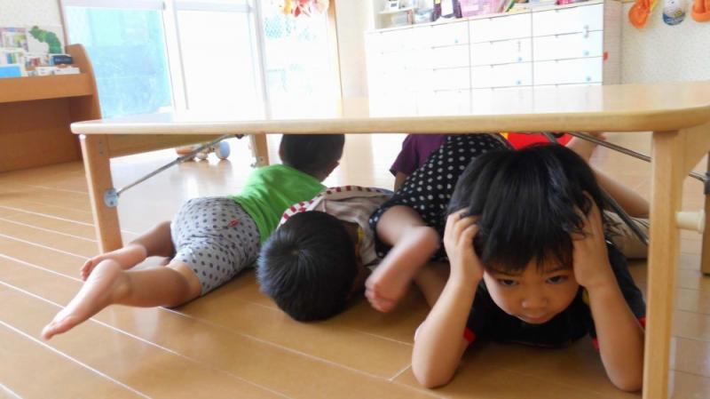防災訓練で机の下に隠れる子どもたち
