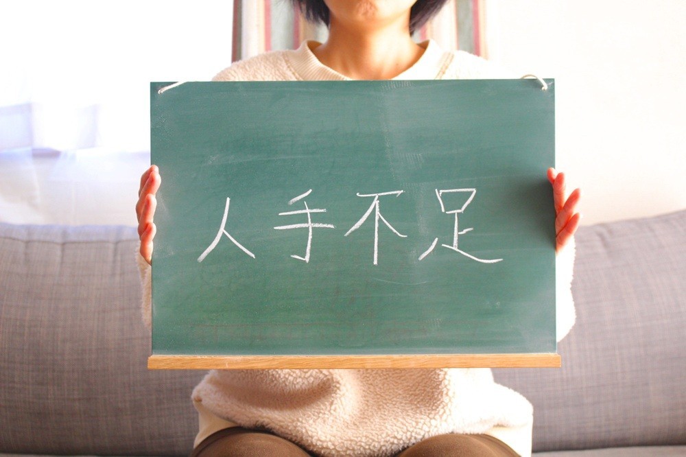 「人手不足」と書かれたボードを掲げる女性