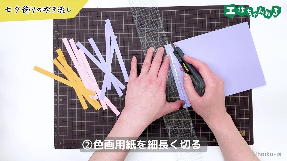 黄色・ピンク・紫の色画用紙をカッターで切っている手元