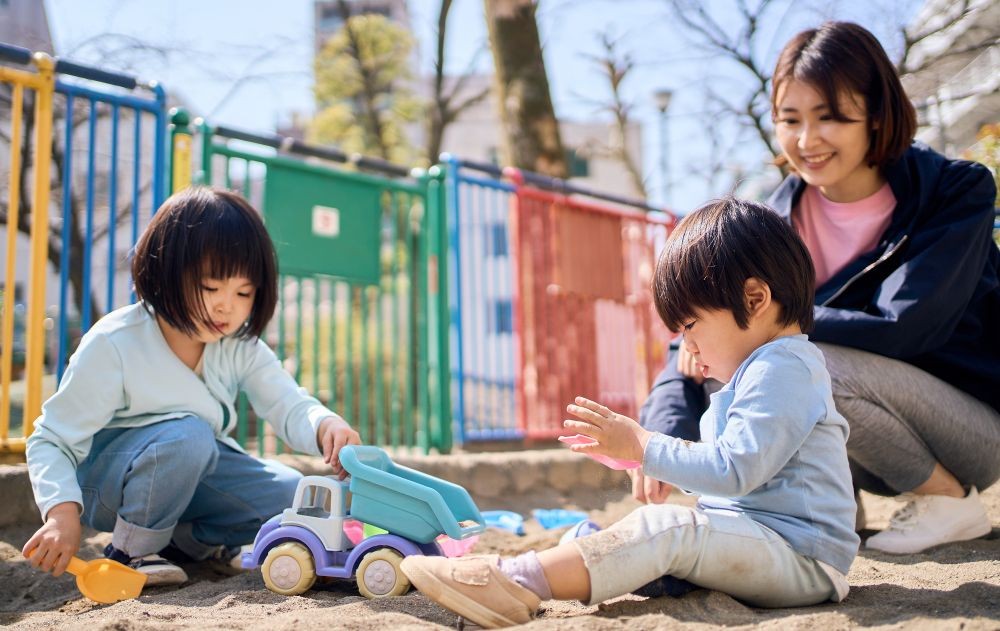 砂場で砂遊びをする子どもたちと見守る保育士