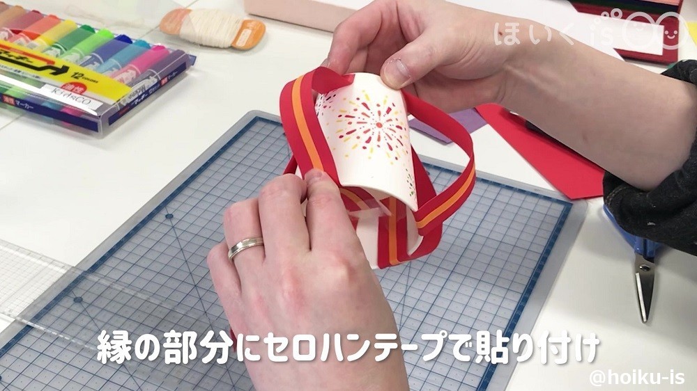 紙コップのフチにセロハンテープで色画用紙を貼り付けているところ
