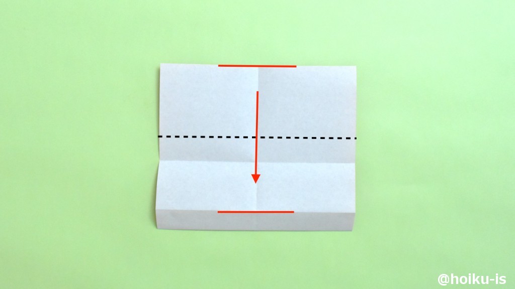 上下の辺（図の2つの赤い線）を合わせるようにして、点線で谷折りにします。