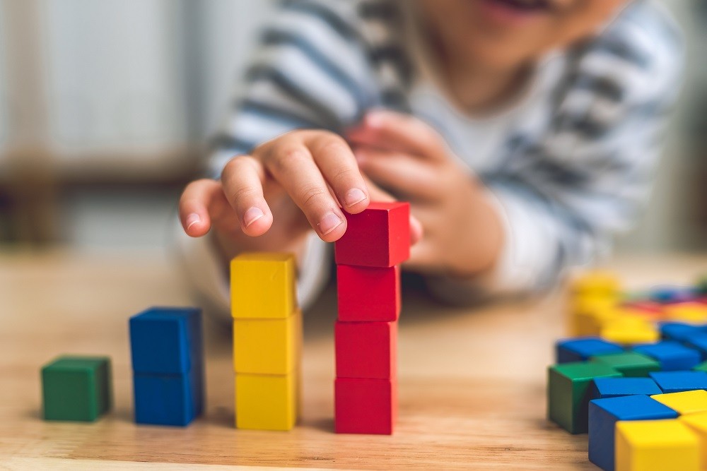赤い積み木を積み重ねている子どもの手