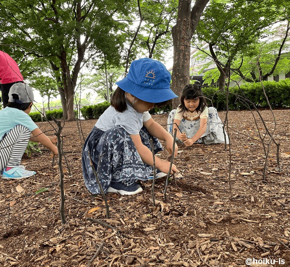 木の枝を地面に指して遊ぶ子どもたち