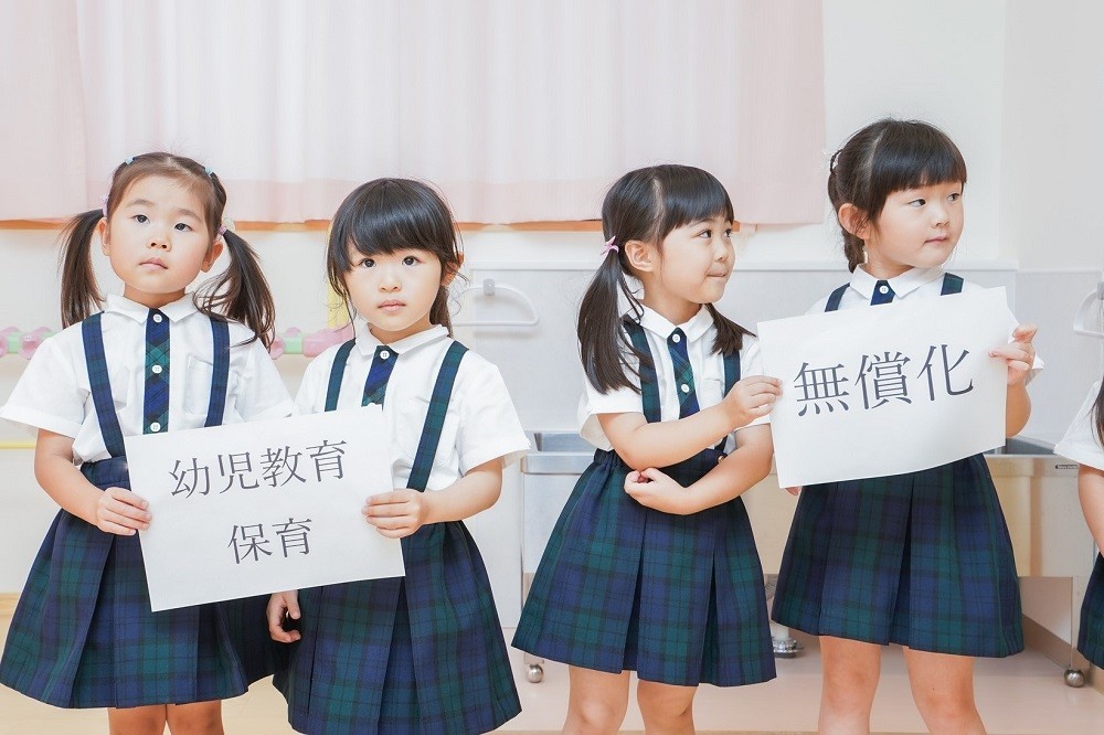 「幼児教育保育の無償化」と書かれたフリップを持った子どもたち