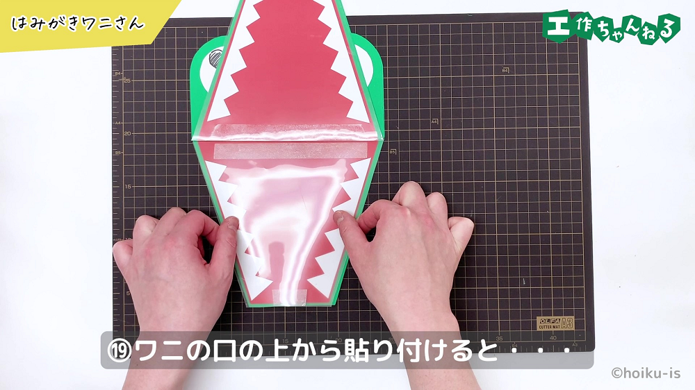 ワニの口にクリアファイルを貼り付けている手元