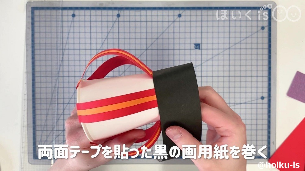 両面テープを貼った黒の画用紙を紙コップに巻き付けているところ