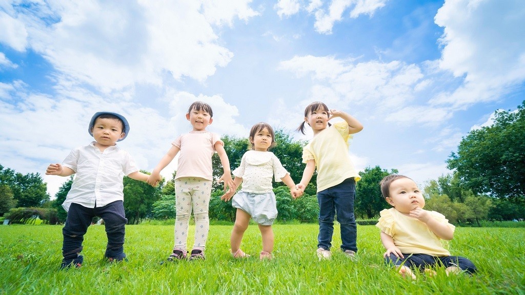 芝生の上でポーズをとる年齢が異なる5人の子ども