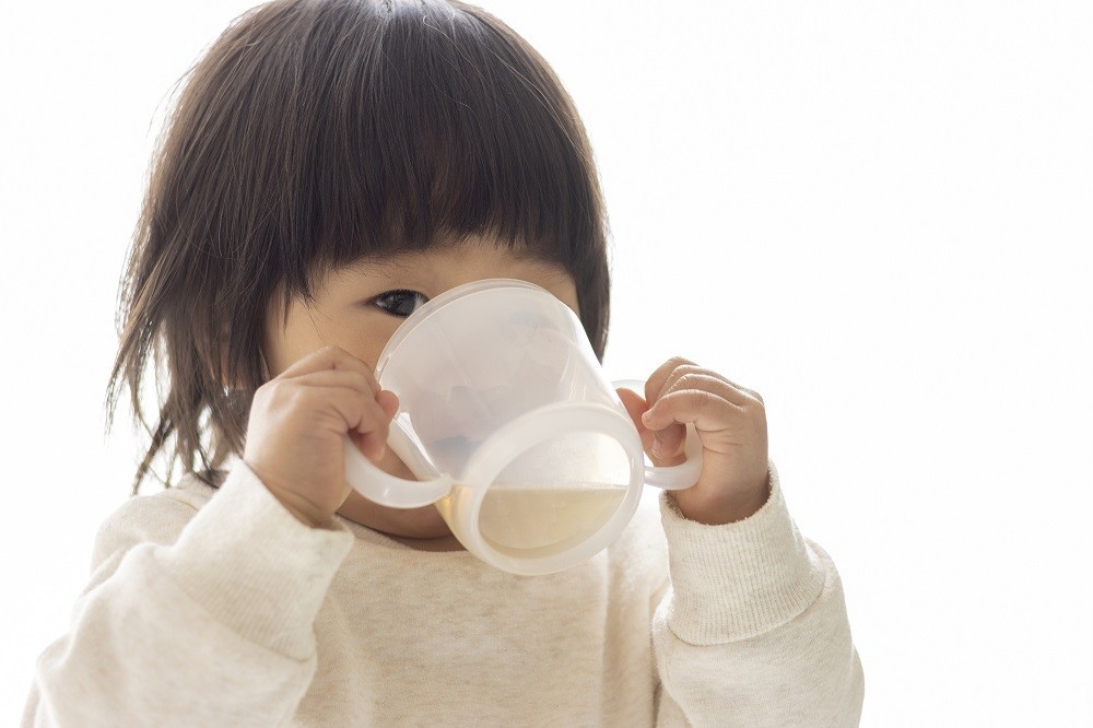 両手でコップを持ってお茶を飲む子ども