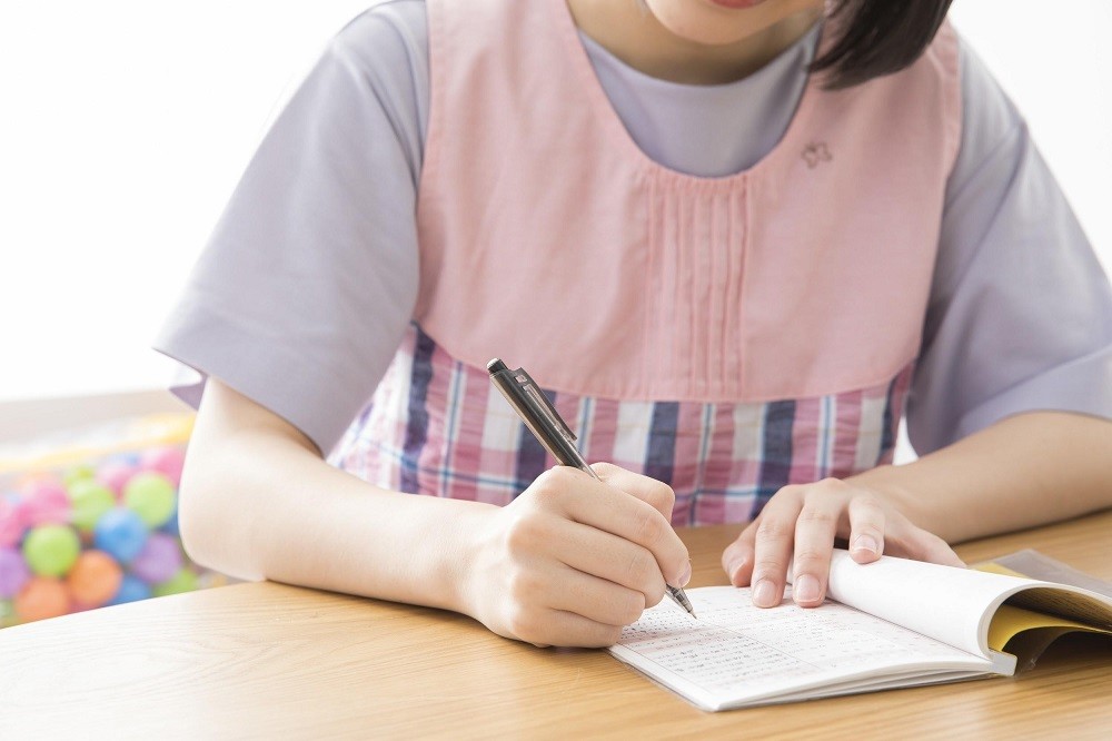 ノートに書きものをしている保育士