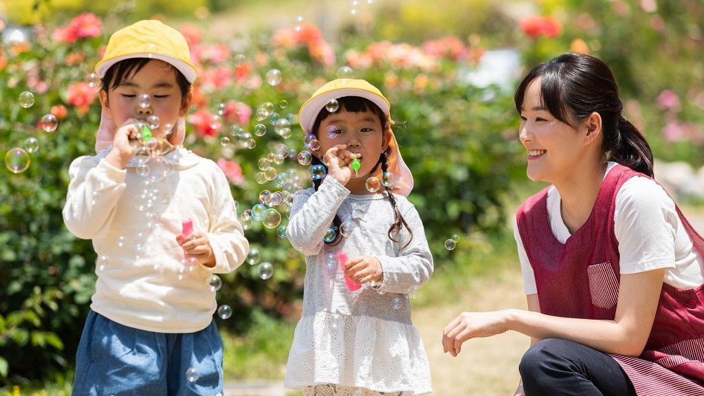 屋外でシャボン玉遊びをする子どもたちと保育士