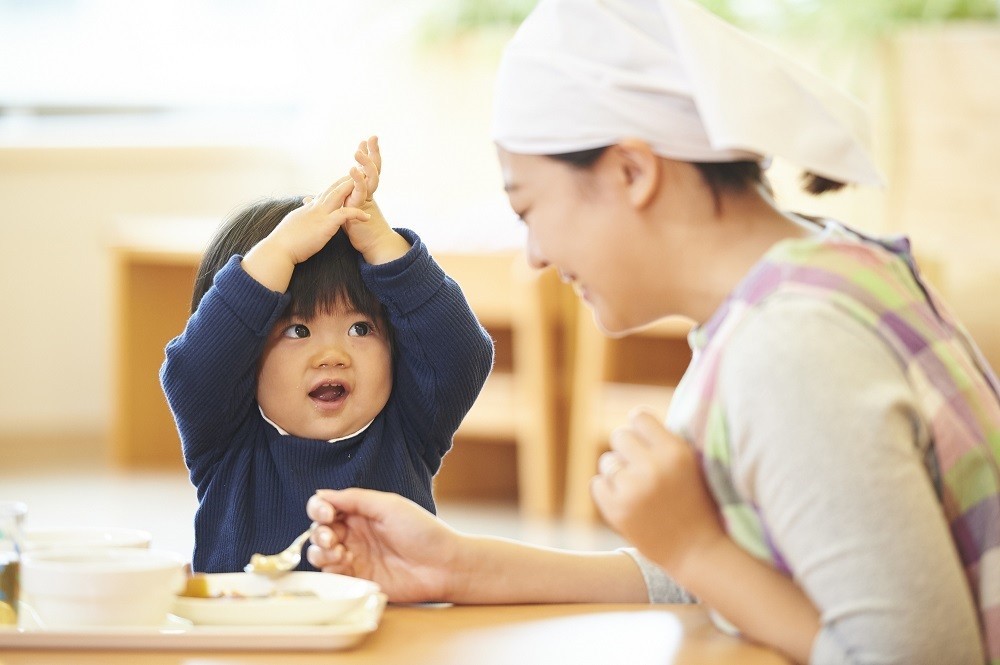 スプーンを持つ保育士と手を上に挙げている子ども