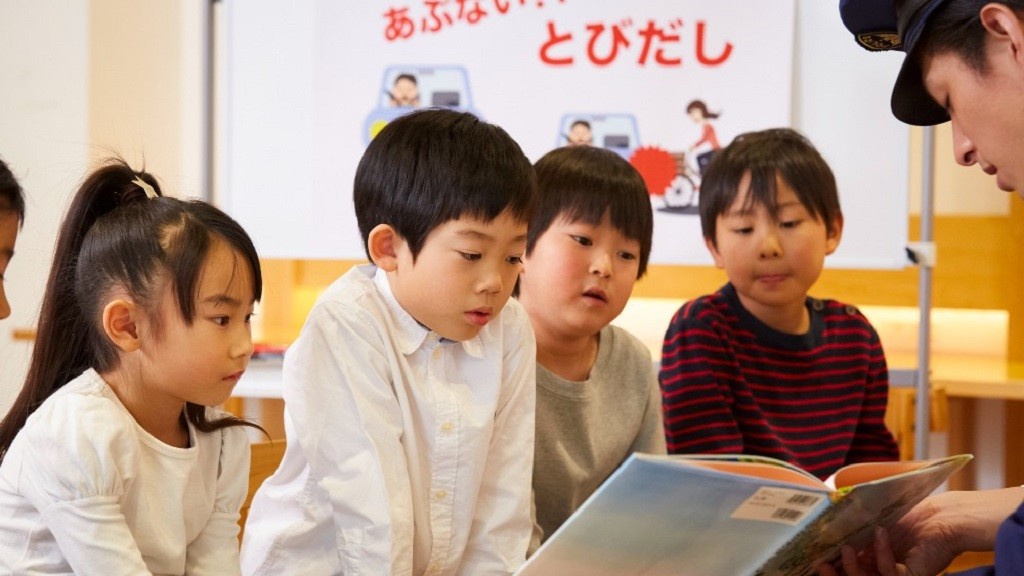 交通安全の絵本を読み聞かせる警察官の話を聞く子どもたち