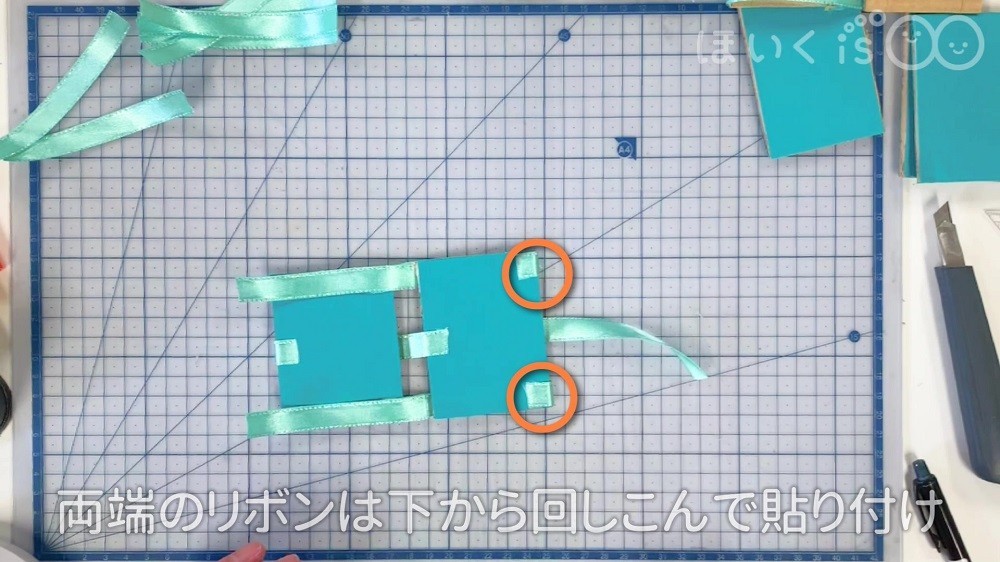 両端のリボンをしたから回しこんで貼り付けている場面