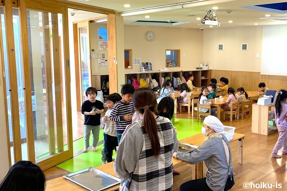 保育室でおやつを受け取るために並ぶ園児たち