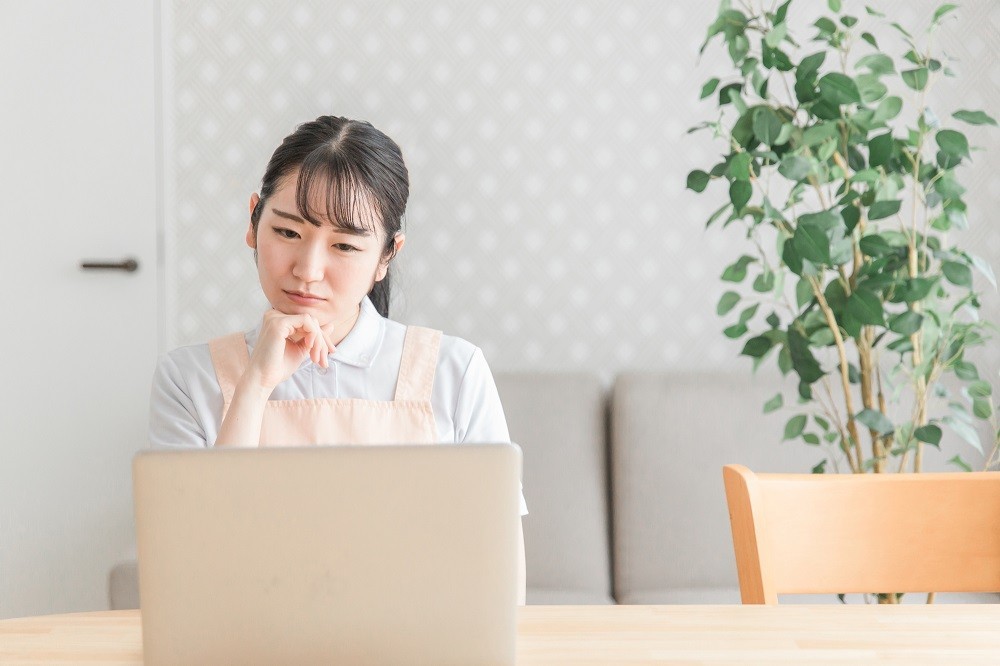 ノートパソコンの前で考え事をする保育士