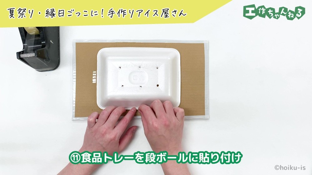 段ボールに食品トレーを貼り付けている手元