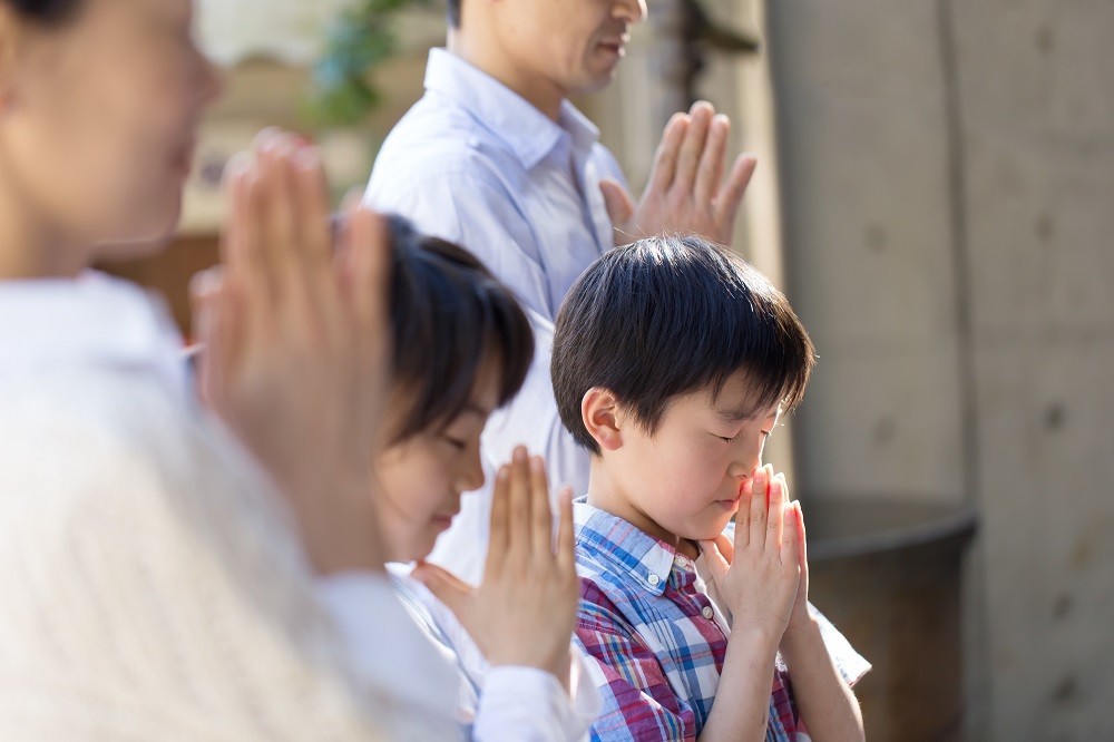 お墓参りで手を合わせる家族