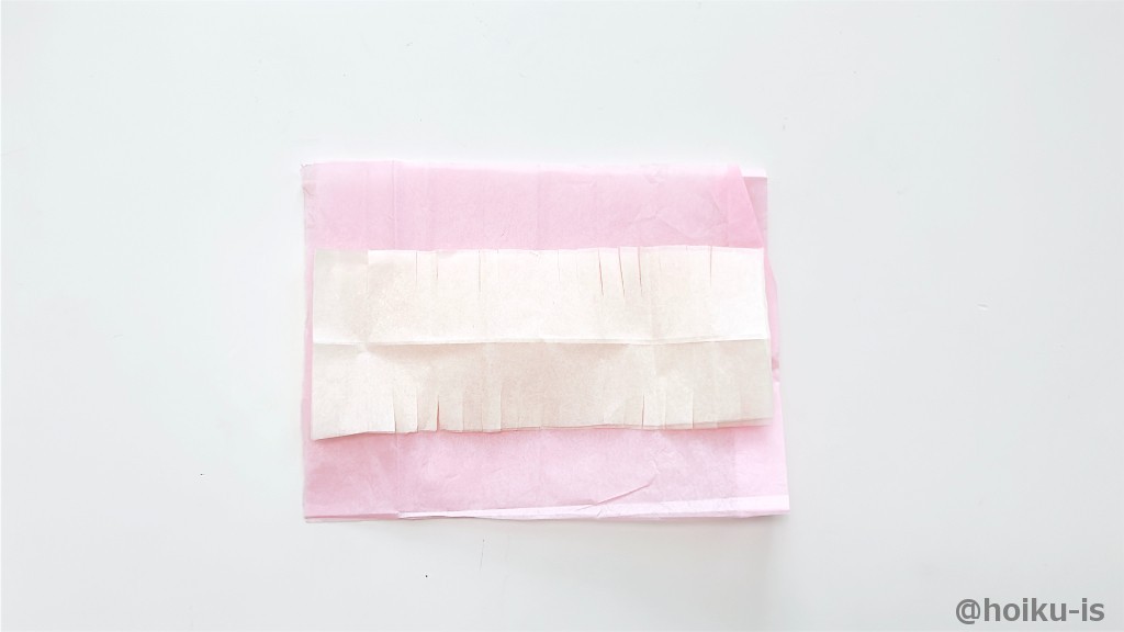 4分の1の薄黄色の花紙をさらに半分に切り、2枚重ねて両端に切り込みを入れる