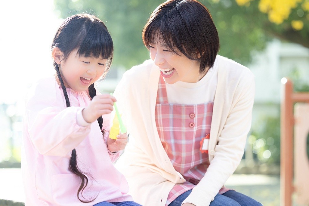 シャボン玉で遊ぶ女の子と保育士