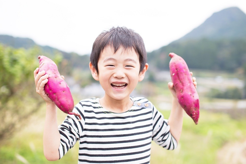 笑顔で両手にさつまいもを持っている子ども