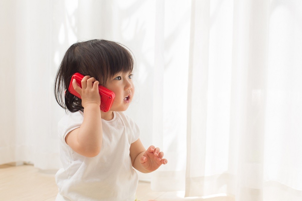 携帯電話のおもちゃを耳に当てている子ども