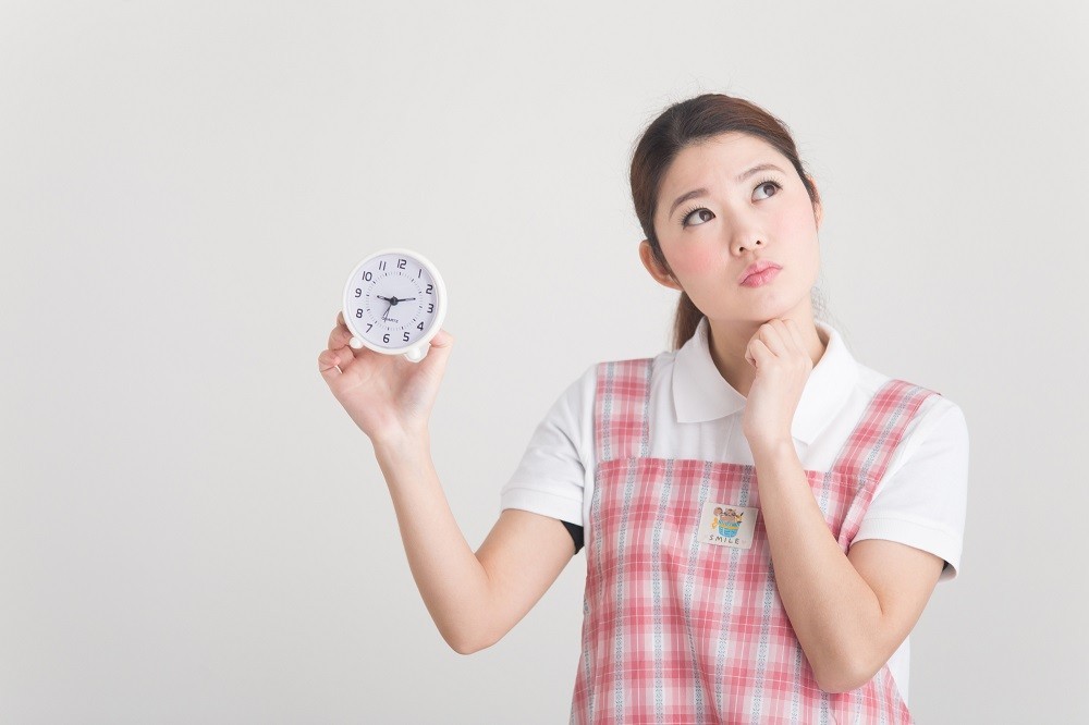 時計を持って考え事をしている保育士