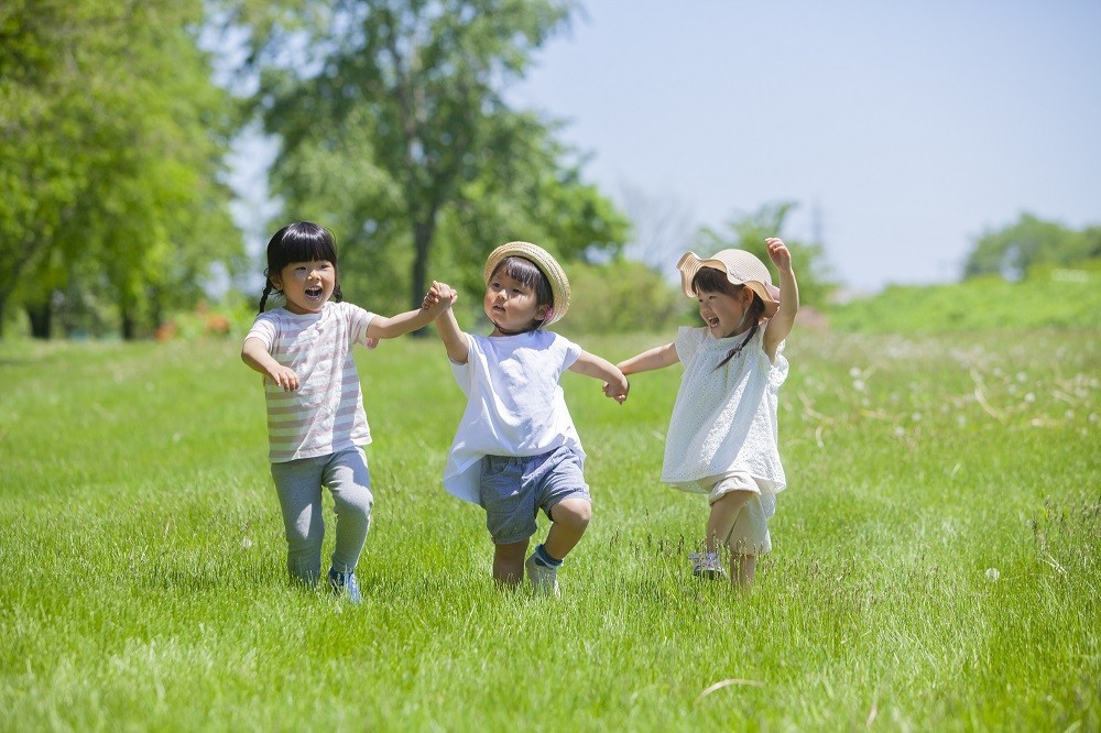 屋外で手を繋いで遊んでいる3人の子ども