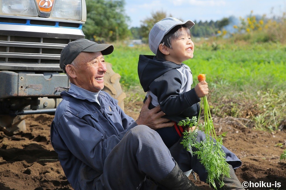 畑で採れたてのニンジンを食べる子どもと農家のおじさん