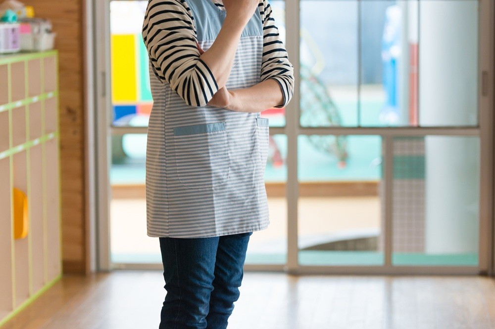 腕を組んで考え事をしている保育士