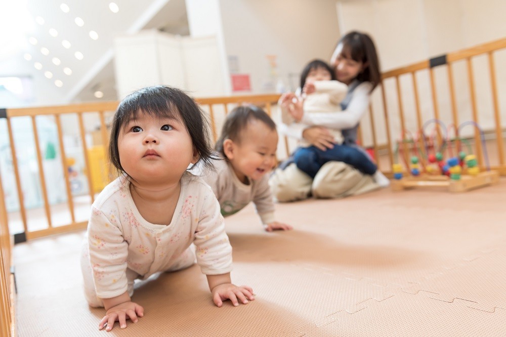 サークルのなかを移動する赤ちゃんと座っている保育士