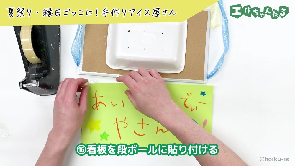 セロハンテープで段ボールに看板を貼り付けている手元