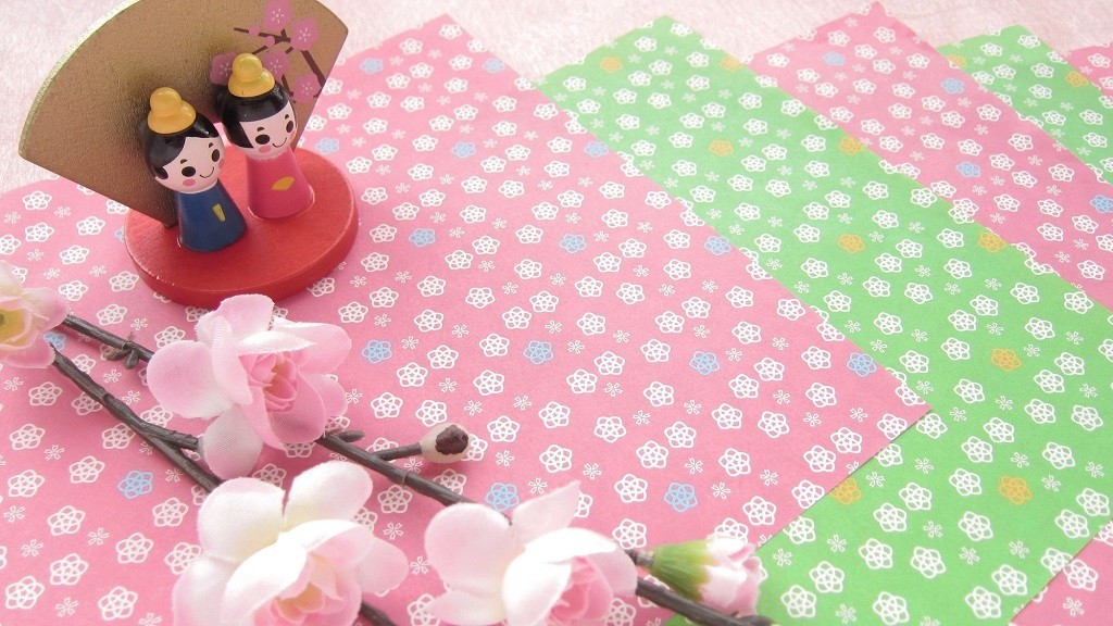 桜の枝と折り紙の上に置かれたひな人形