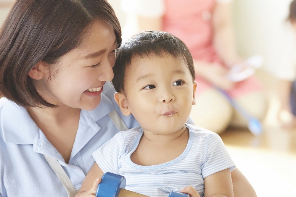 ダンベルのようなおもちゃを持った男の子を抱える保育士