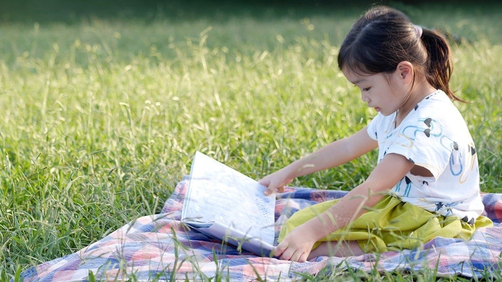 草むらの上で本を読んでいる女の子
