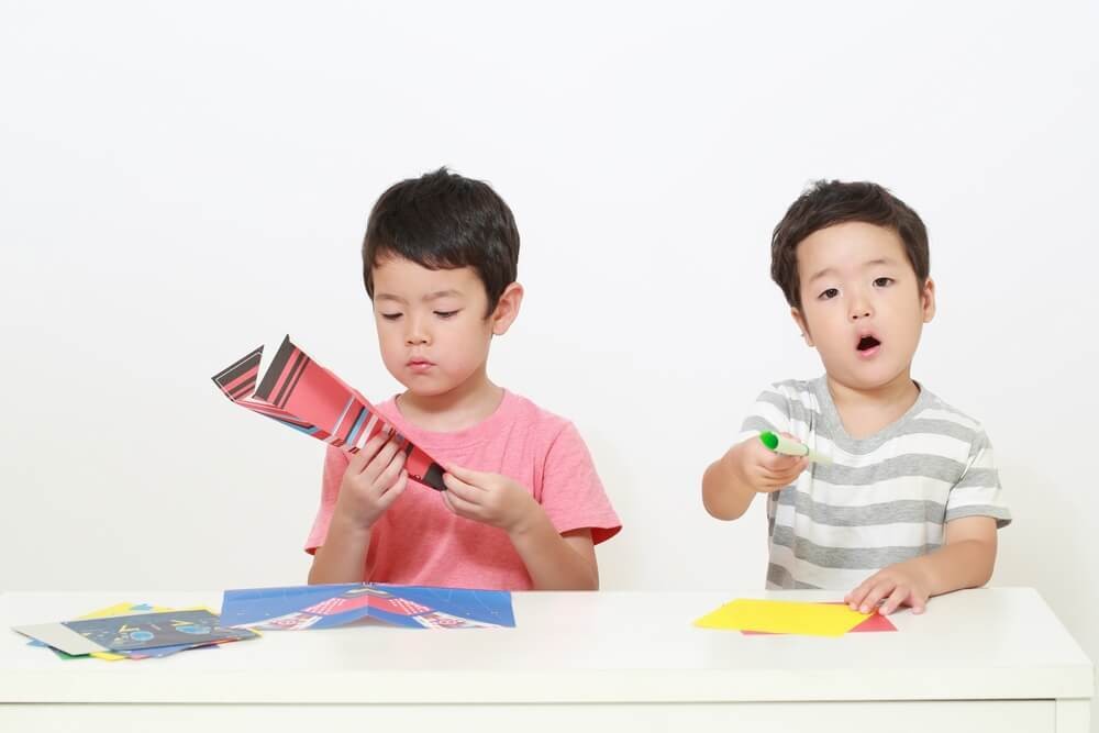 折り紙で紙飛行機を作る子どもたち