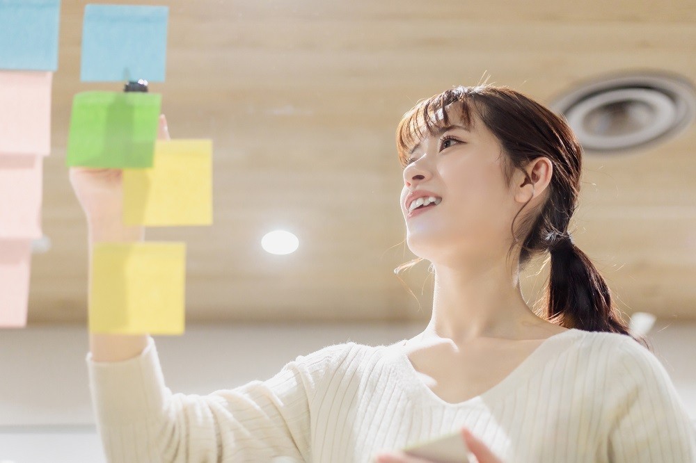 壁に貼られたふせんに書き込みをしている女性