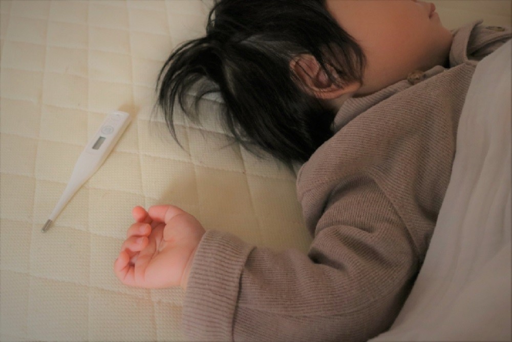 お昼寝をしている小さな子どもと体温計
