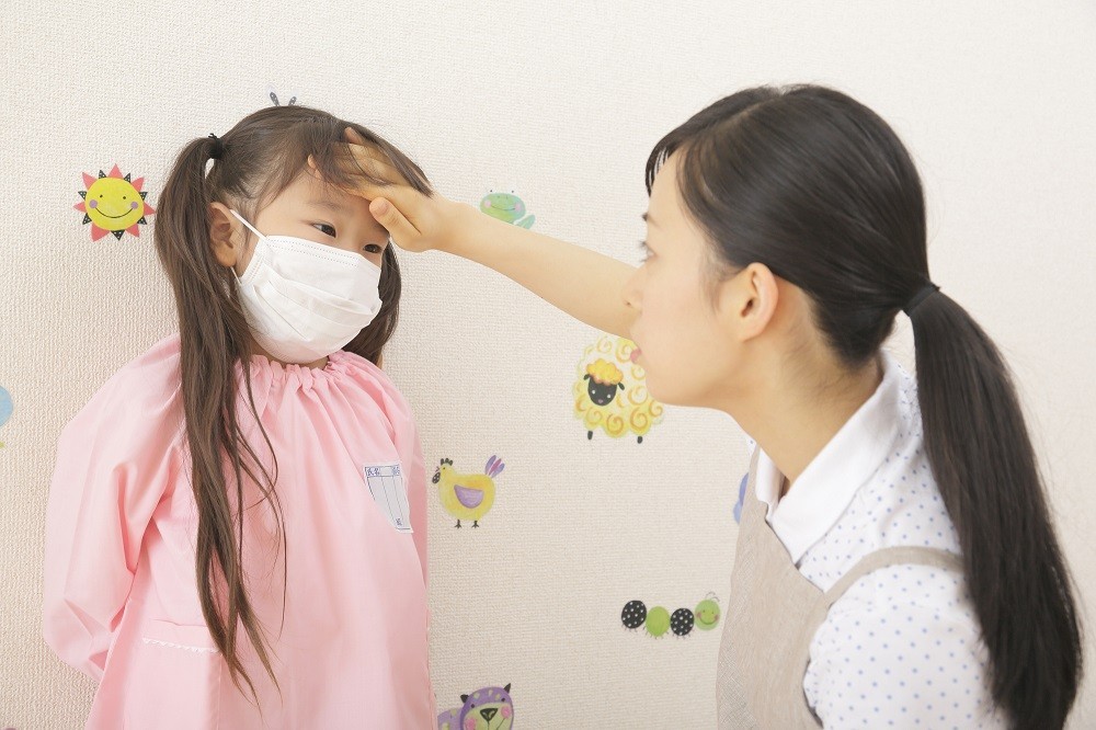 子どものおでこに手を当てる保育士