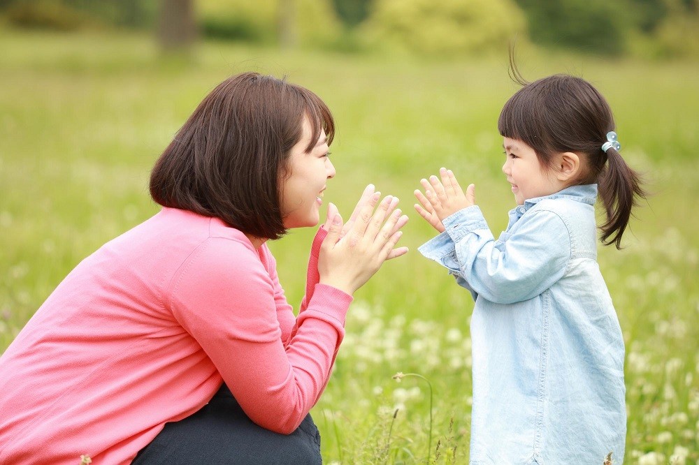 野原で手遊びをする女性と女の子