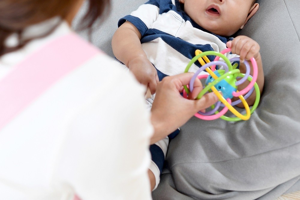 横になった状態でおもちゃを持つ赤ちゃん