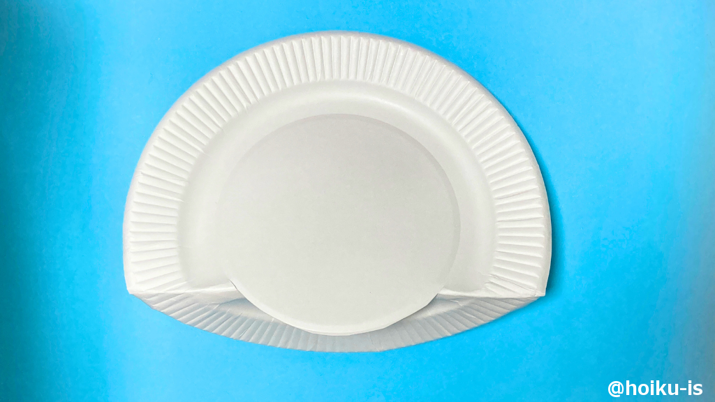 紙皿の真ん中の円の下側をカッターで切り、切った部分の左右を折る。