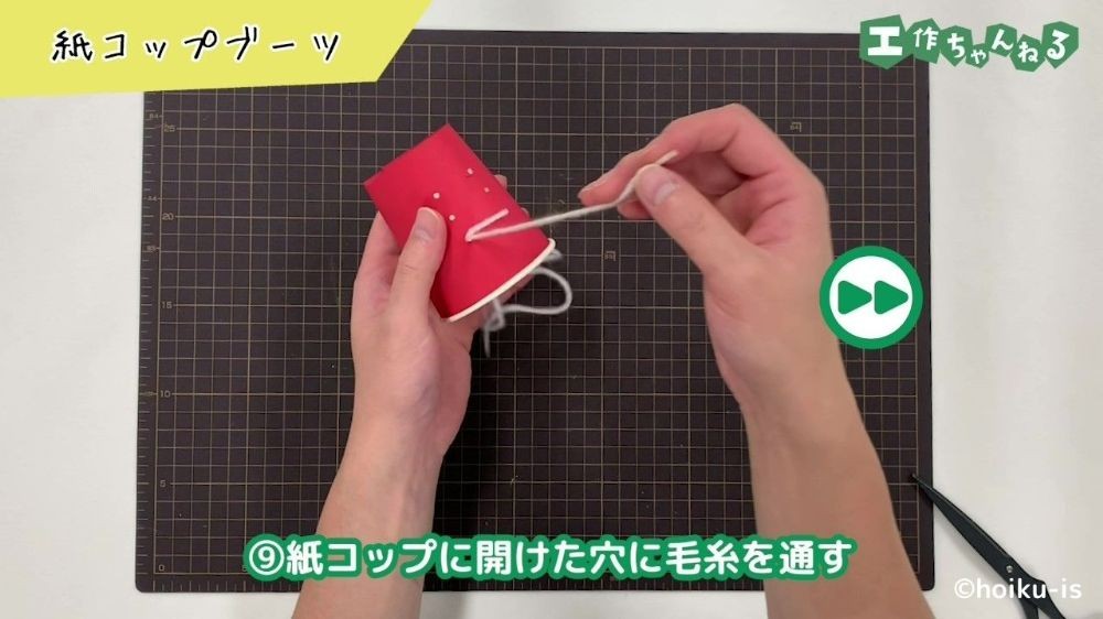 紙コップに開けた穴に毛糸を通している手元