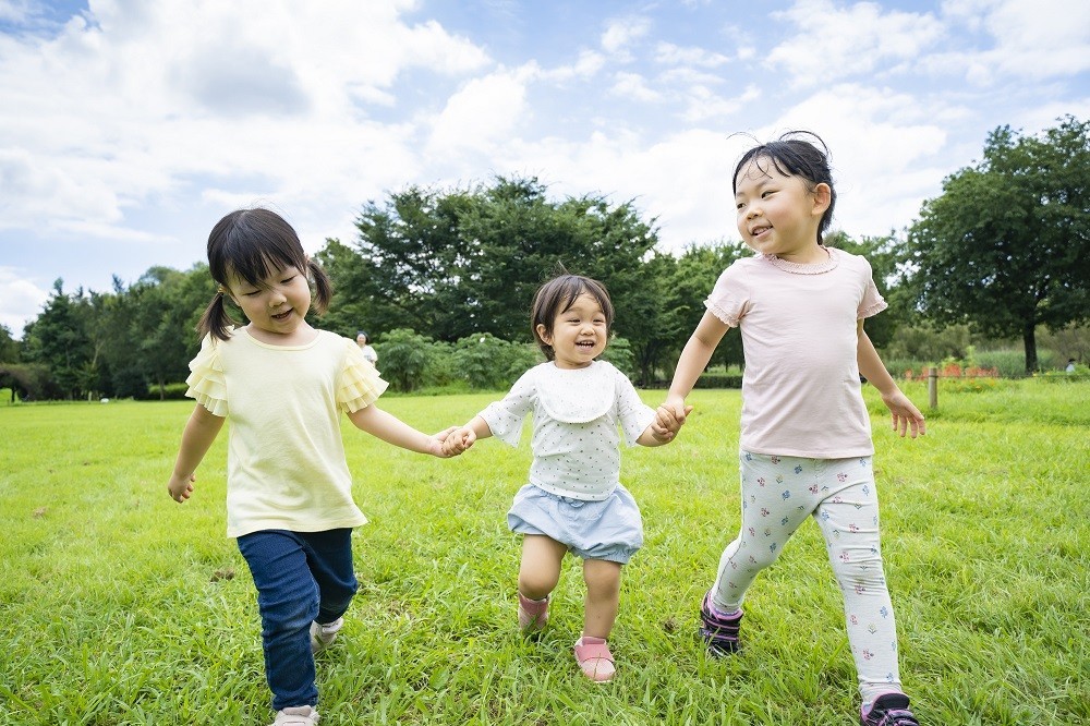 手をつないで芝生を歩く3人の子ども