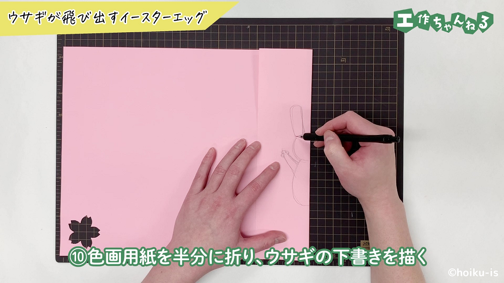 ピンクの画用紙にうさぎの下書きを描いている手元