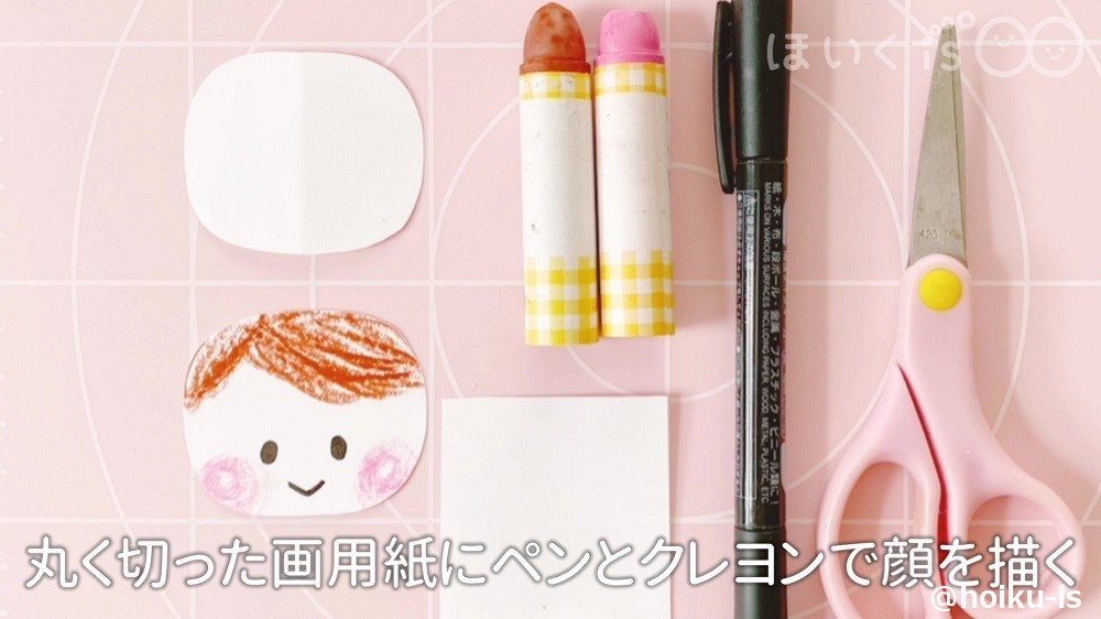 丸く切った画用紙にペンとクレヨンで顔を描いているところ
