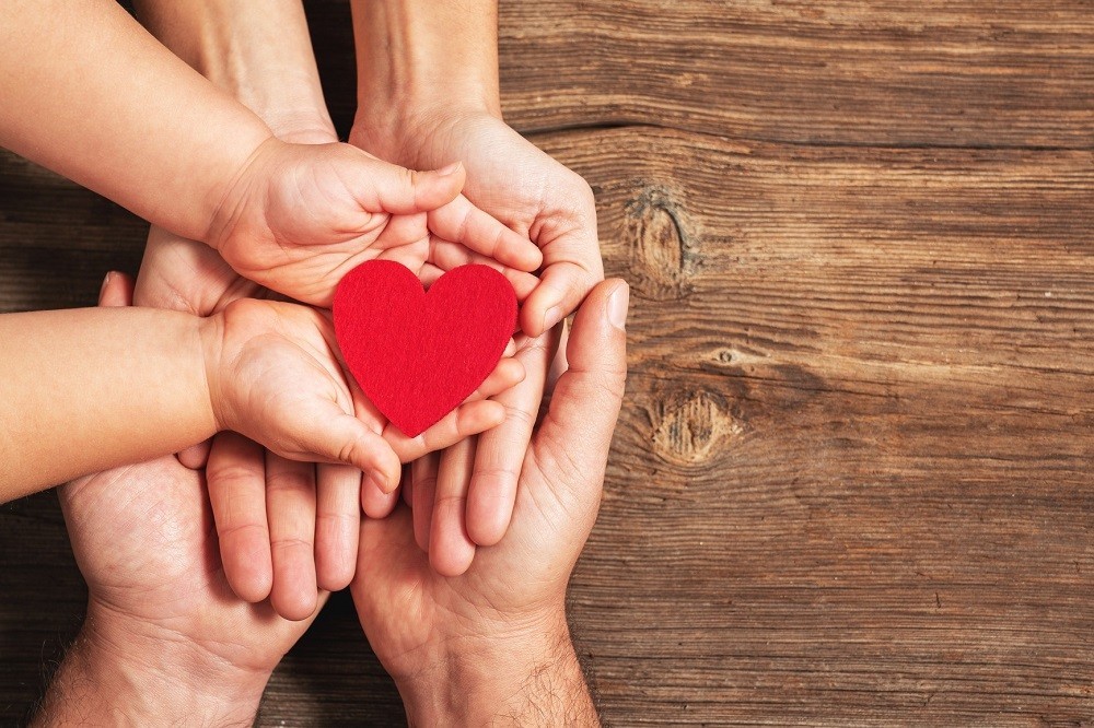 子どもと大人の掌の上に乗った赤いハートの積み木