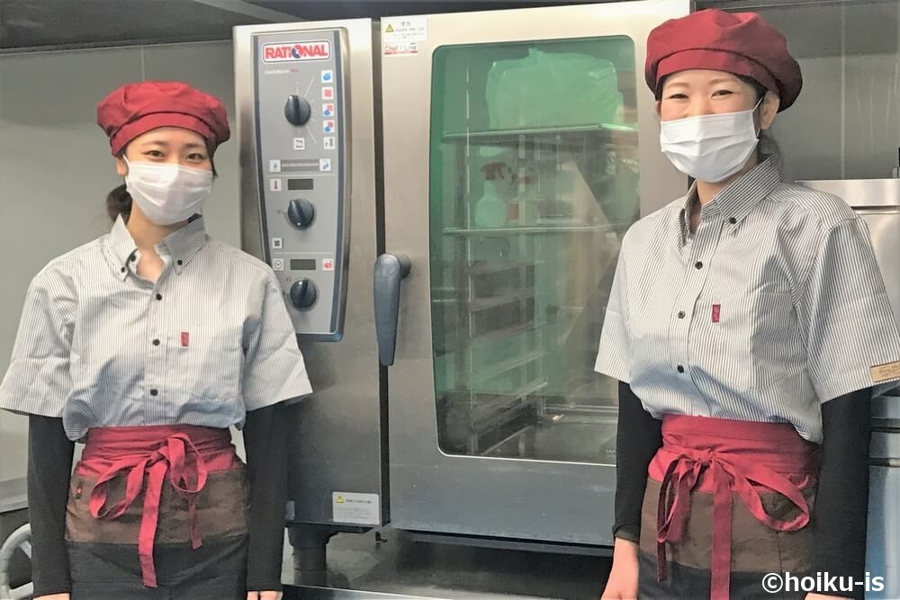 調理室の中で立っている給食調理スタッフの女性