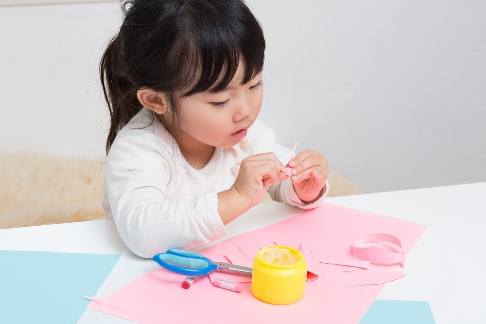 画用紙とハサミとのりを使って工作をしている女の子