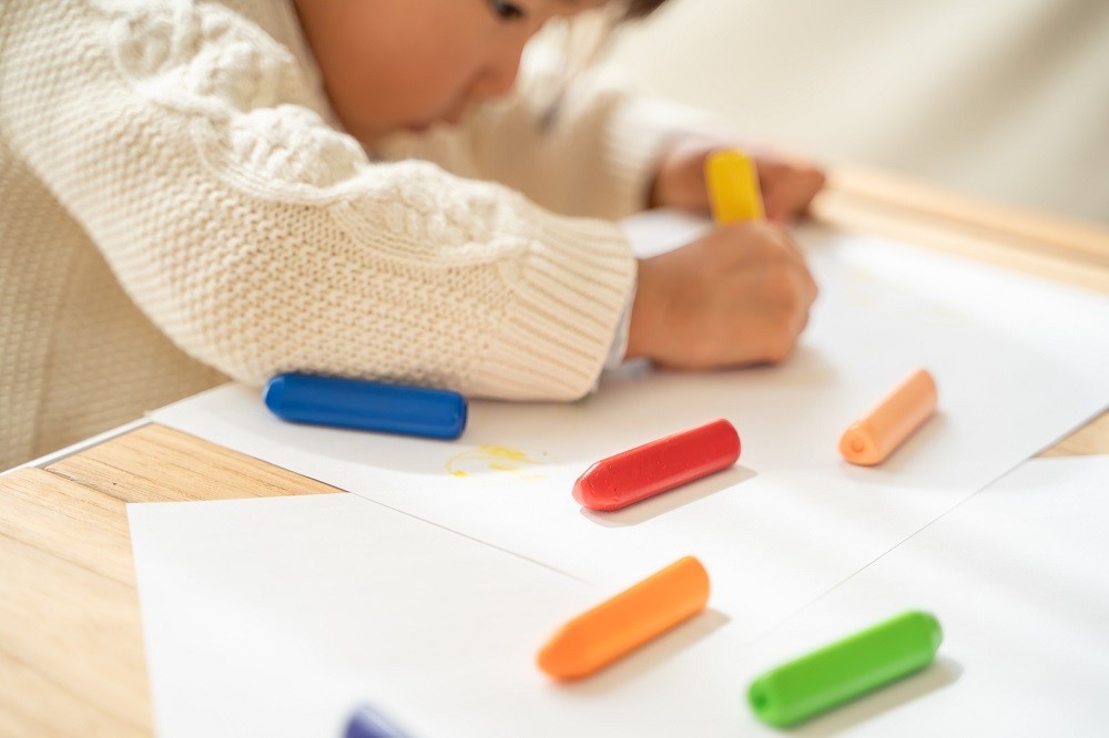 クレヨンでのお絵描きに夢中になっている子ども